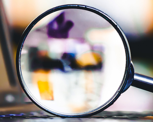 A magnifying glass sits atop a laptop keyboard. Learn about Pedal Point Solutions testing services