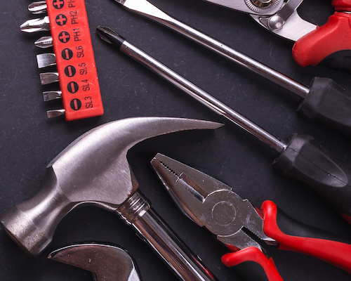 A hammer, pliers, screwdriver and other tools laying on a black table. Learn about tools from Pedal Point Solutions