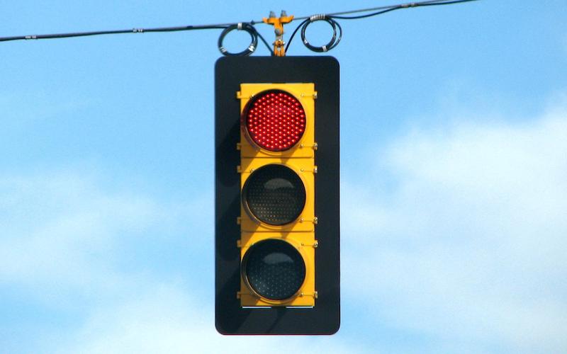 A stoplight with the red light lit hangs from a wire against the backdrop of a blue sky