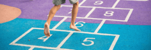 A boy's legs skip across the numbered squares of a pink and blue hopscotch board