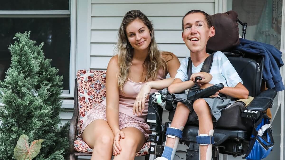 Hannah Aylward and Shane Burcaw (a.k.a. Squirmy and Grubs) smile as they sit together in front of a house