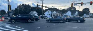 Cars zoom through a busy intersection with a brightly painted crosswalk and overhanging set of stoplights