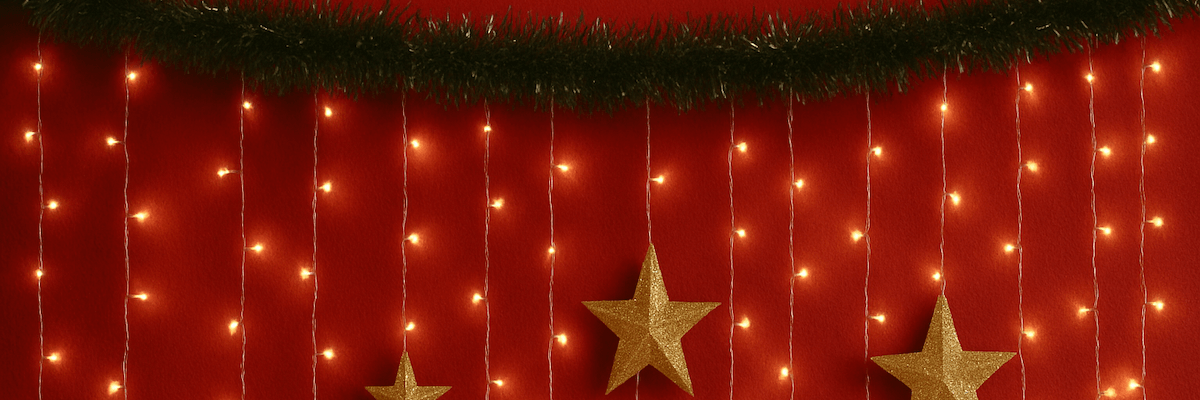 Festive tinsel, twinkly lights, and golden stars hang on a red wall