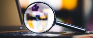 A magnifying glass sits atop a laptop's keyboard. The image within the magnifying glass is blurred.