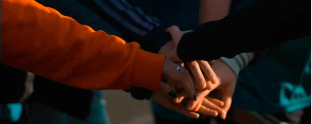 Close-up of a diverse group of people stacking hands in a show of teamwork and unity, lit warmly against a shadowed background.