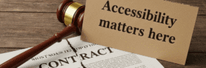 A sign reading “Accessibility matters here” rests on top of a torn contract and a partially visible judge’s gavel. The contract is ripped down the middle.