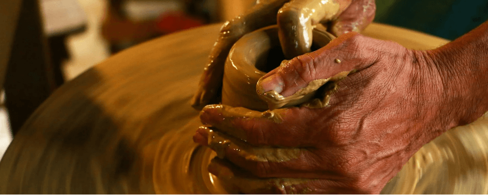 Close-up of a pair of hands shaping clay on a spinning pottery wheel.