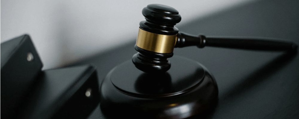 A black and gold gavel rests on a shiny black table next to a pile of legal binders