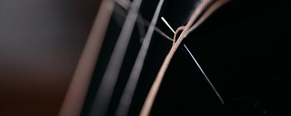 A needle twisting amidst four thick threads against a dark background.