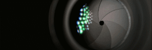 Extreme closeup of a camera shutter almost fully closed behind a lens reflecting colored lights