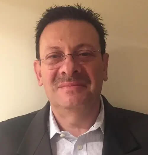 Igor Feinberg, a middle-aged man with dark hair and glasses, wears a blazer and white shirt standing against a soft beige background.